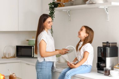 Mutfakta bulaşık yıkayan küçük kızıyla mutlu bir anne.