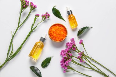 Güzel çiçekli kozmetik yağı şişeleri ve beyaz arka planda deniz tuzu.