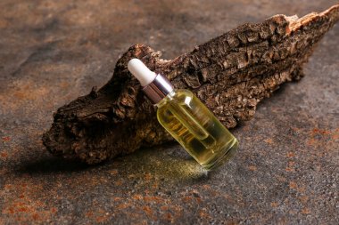 Koyu arkaplanda ağaç kabuğu olan bir şişe kozmetik yağı.