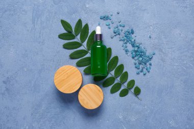 Mavi arka planda deniz tuzu bulunan şişe ve kozmetik ürünleri.