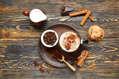 Tarçınlı bir fincan lezzetli kahve, ahşap arka planda fasulye ve kurabiye.