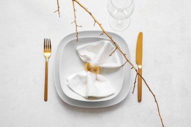 Altın çatal bıçak takımı, katlanmış peçete ve ağaç dalı beyaz arka planda.