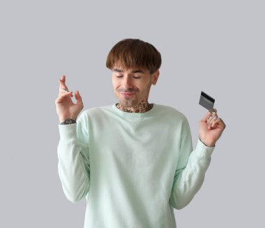 Kredi kartı ile dövmeli genç bir adam ışık arka planda şans diliyor.