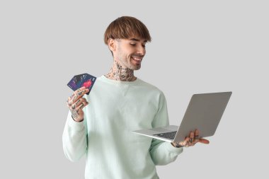 Kredi kartı ve dizüstü bilgisayarı olan dövmeli genç bir adam.