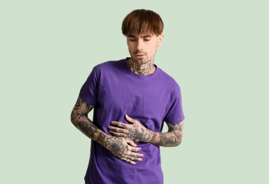 Yeşil arka planda karın ağrısı çeken genç bir adam.