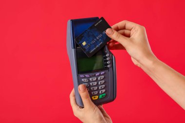 Kırmızı arka planda kredi kartıyla ödeme yapan genç kadın, yakın plan.