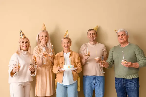 Mature people with cake and champagne celebrating Birthday on beige background