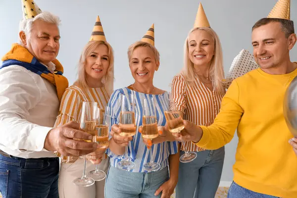 Mature people with glasses of champagne celebrating Birthday on light background