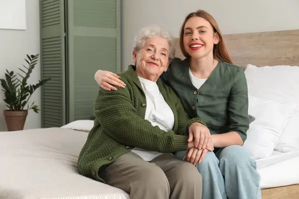 Young woman with her grandmother hugging in bedroom
