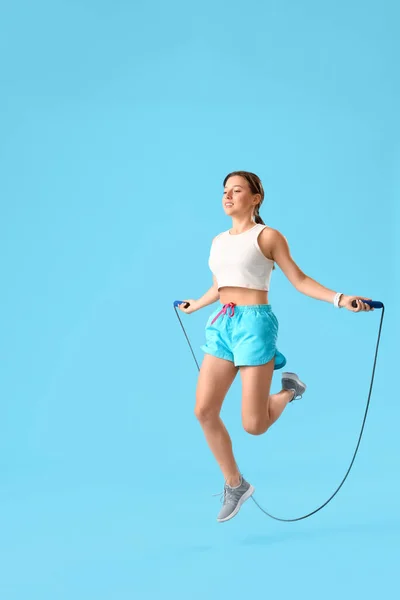 Sporty young woman jumping rope on blue background