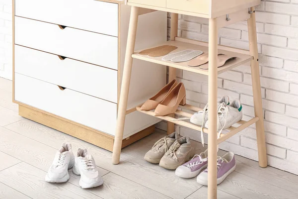 Shoe rack with stylish shoes and orthopedic insoles near light brick wall in room