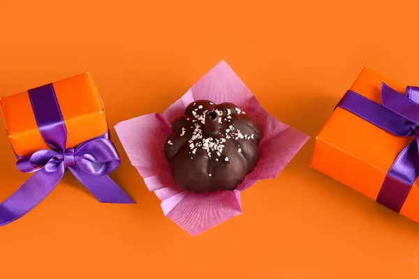 Delicious chocolate cake and gift boxes for Halloween celebration on orange background