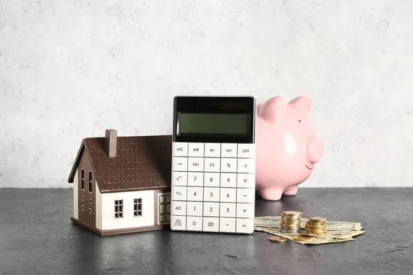 Calculator with piggy bank, house model and money on black table