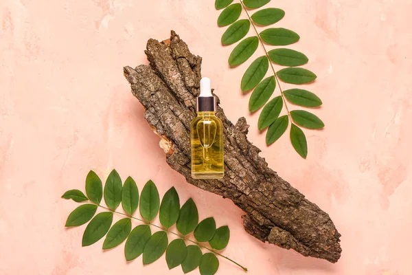 Bottle of cosmetic oil with tree bark and leaves on pink background