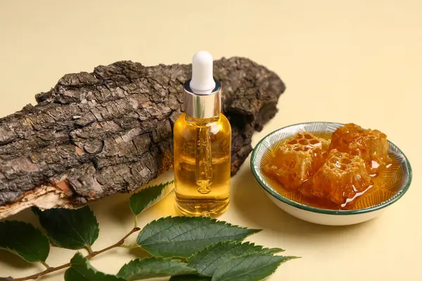 Bottle of cosmetic oil with honey and leaves on yellow background