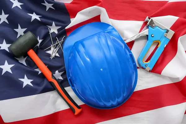 Hardhat, rubber mallet and industrial stapler on USA flag. Labor Day celebration