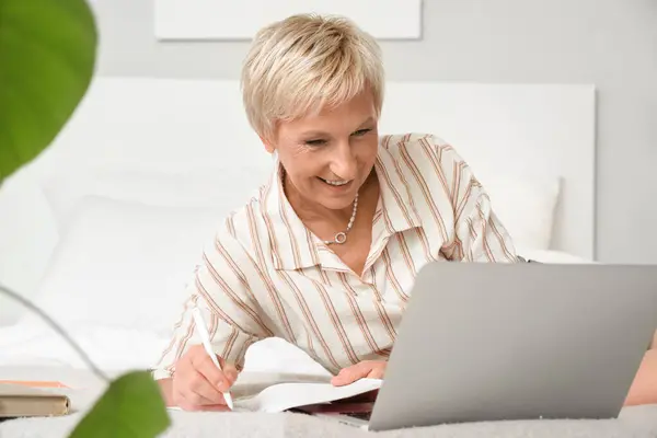 Mature woman learning English language online in bedroom