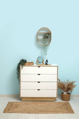 Hasır halı, çekmece sandığı ve vazoda otlar olan oturma odasının içinde.