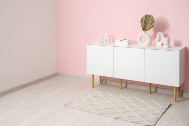 Şık bir halı ve pembe duvarın yanındaki beyaz büfe.