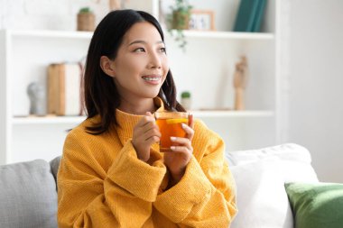 Evdeki oturma odasında bir fincan çayla güzel bir Asyalı kadın.