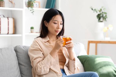 Oturma odasındaki kanepede çay içen güzel, genç Asyalı kadın.