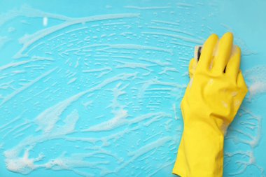Sarı lastik eldivenli bir kadın, mavi yüzeyi süngerle temizliyor.