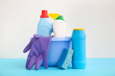 Plastik kasede beyaz arka planda deterjan, sünger ve eldivenler var.