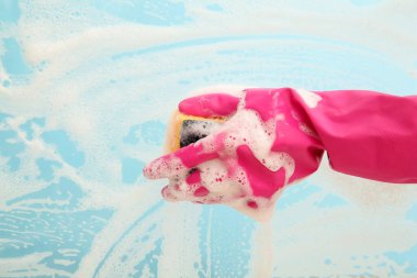 Pembe lastik eldivenli bir kadın, mavi yüzeyi süngerle temizliyor.