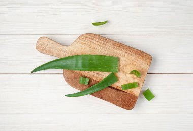 Aloe vera yapraklarıyla beyaz ahşap arka planda kesim tahtası