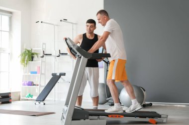 Rehabilitasyon merkezinde terapistle koşu bandında çalışan olgun bir adam.