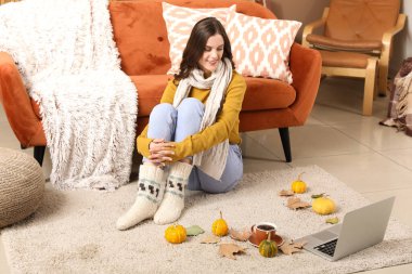 Sonbahar günü dizüstü bilgisayarı olan genç bir kadın evde oturuyor.