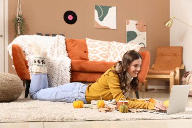 Sonbahar günü evde dizüstü bilgisayar kullanan genç bir kadın.