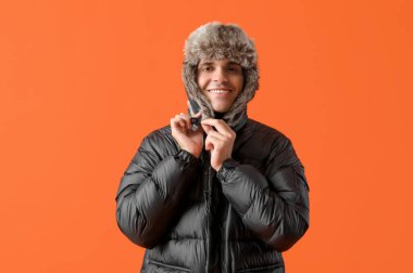 Turuncu arka planda kışlık elbiseli genç adam.