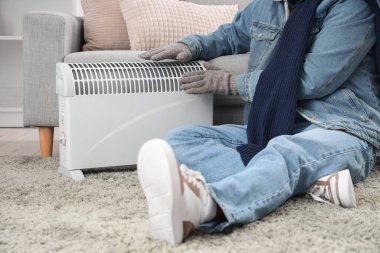 Genç adam radyatörün yanında ısınıyor, yakın çekim.