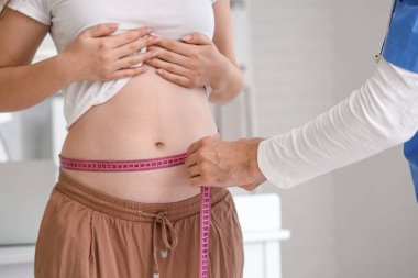 Klinikte genç hamile bir kadının karnını ölçen erkek doktor, yakın plan.