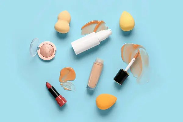 Bottles of makeup foundation with samples and decorative cosmetics on blue background