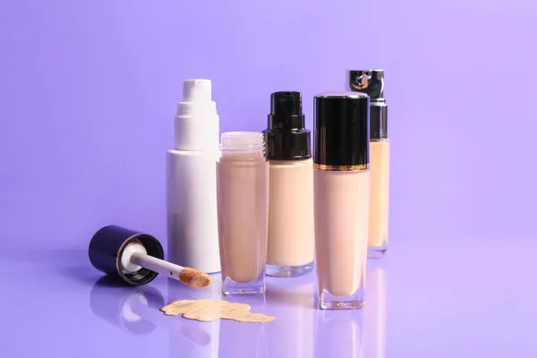 Bottles of makeup foundation with sample on purple background