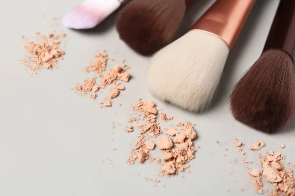 Makeup brushes and facial powder on grey background