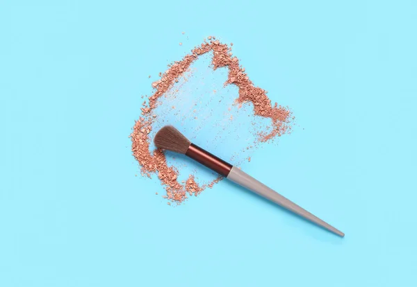 Makeup brush and highlighter on blue background