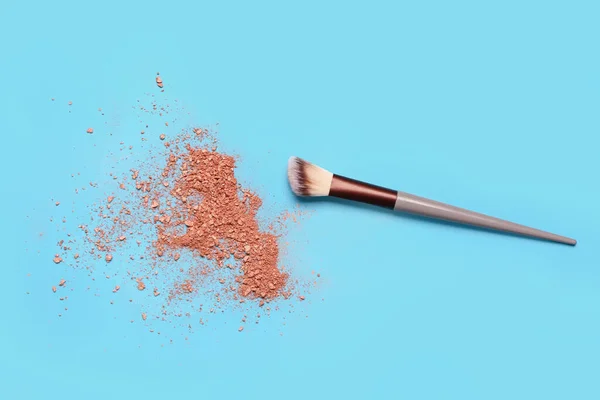 Makeup brush and highlighter on blue background