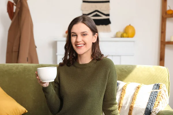 Sonbahar günü elinde bir fincan çayla evde oturan genç bir kadın.