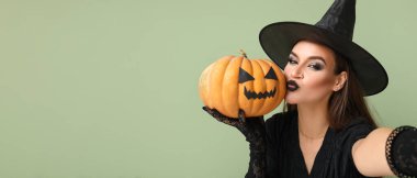 Cadılar Bayramı için balkabaklı cadı gibi giyinmiş genç bir kadın yeşil arka planda selfie çekiyor ve mesaj için yer var.