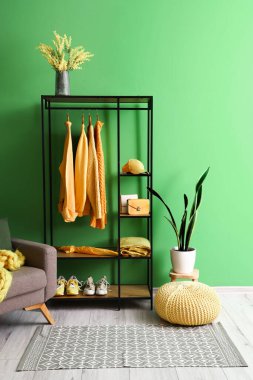 Odadaki yeşil duvarın yanında giysi ve aksesuarlı raf ünitesi.