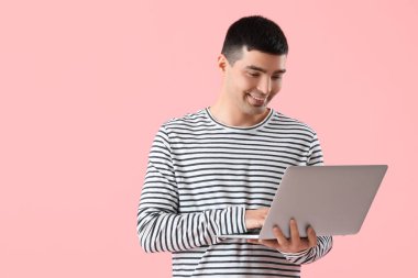 Pembe arka planda dizüstü bilgisayarı olan genç bir adam.