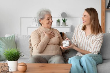 Evde büyükannesini hediyeyle selamlayan genç bir kadın.