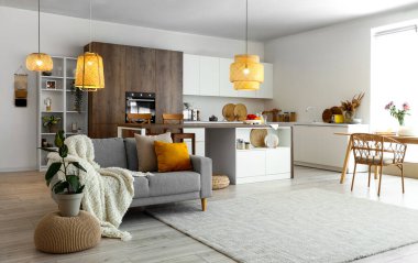 Modern açık mutfak, yemek masası, ada, gri kanepe ve parlayan lambalar.