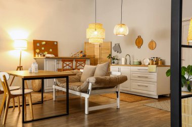 Parlayan lambalar, yemek masası, kanepe ve akşamları beyaz tezgahlı modern mutfak.