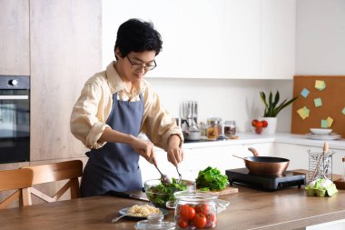 Genç Asyalı adam mutfakta sebze salatası yapıyor.