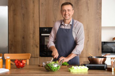 Olgun bir adam mutfakta marul kesiyor.