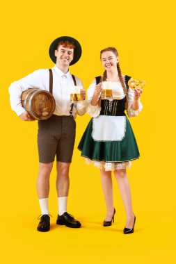Geleneksel Alman kıyafetleri içinde, sarı arka planda bira ve simit olan genç bir çift.